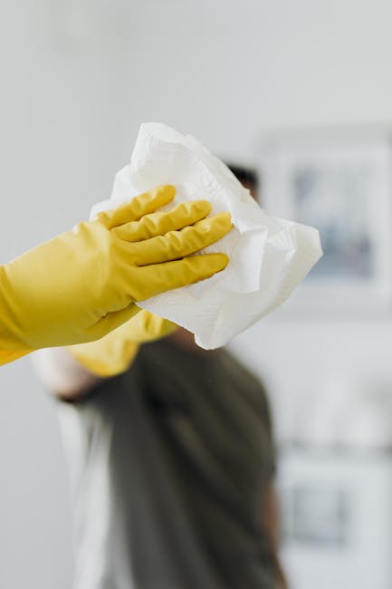 A professional cleaner from Carpet Cleaning Chiswick, dressed in a grey t-shirt and bright red overalls, is engaged in surface cleaning within a modern kitchen. He is using a handheld cleaning tool on